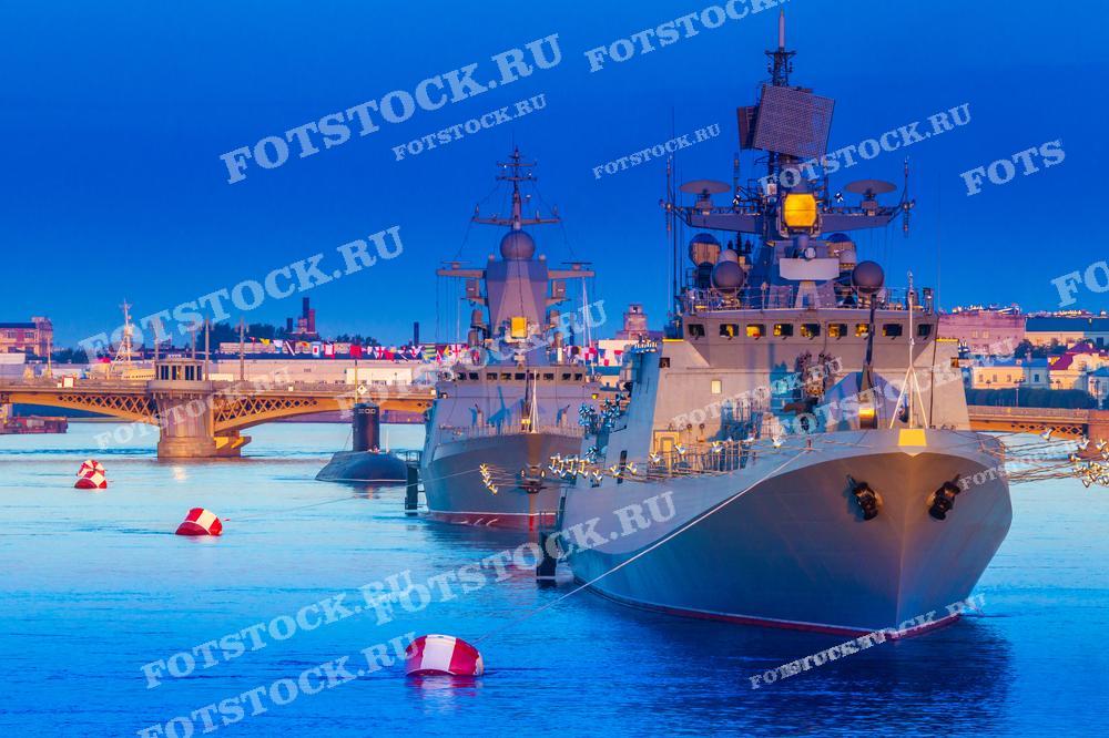 На снимке мы видим военные корабли в акватории реки Невы. Отражения освещения на воде создают красочную и яркую картину. 
Фотография подходит для публикаций, связанных с военно-морской тематикой, описаний парадов и празднований дня ВМФ.